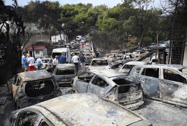 People stand amid the charred remains of burned-out cars following a deadly wildfire, in Mati east of Athens, Tuesday, July 24, 2018. (AP Photo/Thanassis Stavrakis, File)