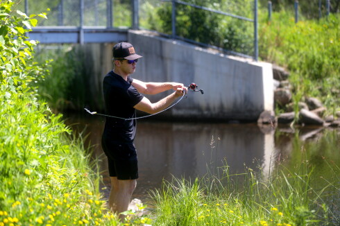 A fishing rod bending as a man makes a cast at a pond.