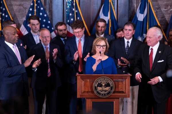 Newly appointed U.S. interim Senator, Darline Graham Nordone, with South Carolina Gov. Henry McMaster, right, and Sen. Time Scott (R-SC), left, speaks to members of the press after being appointed of to fill the vacancy created by the passing of her brother, U.S. Senator Lindsey Graham, at the statehouse Monday, July 13, 2026, in Columbia, S.C. (AP Photo/Sean Rayford)