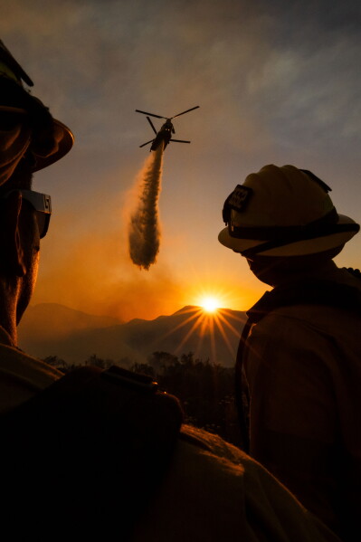 Firefighters watch as a helicopter drops water on the Summit Fire in Llano, CA. Friday, July 10, 2026. (AP Photo/Ethan Swope)
