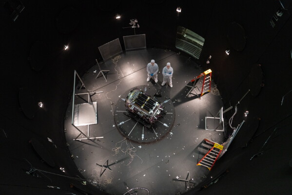 This photo provided by NASA shows Kieran Wilson, LINK’s principal investigator, and Hunter Robertson, a space systems engineer, both at Katalyst Space, standing next to their spacecraft inside the SES (Space Environment Simulator) at NASA’s Goddard Space Flight Center in Greenbelt, Md., April 17, 2026, ahead of thermal vacuum testing. (Sophia Roberts/NASA via AP)
