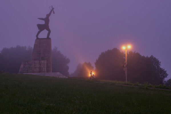 A couple stand near the monument "Peremilovskaya Heights", in Peremilovo village, about 70 kilometers ( 44 miles) north from Moscow, Russia, before sunrise, Sunday, July 12, 2026. (AP Photo/Alexander Zemlianichenko)