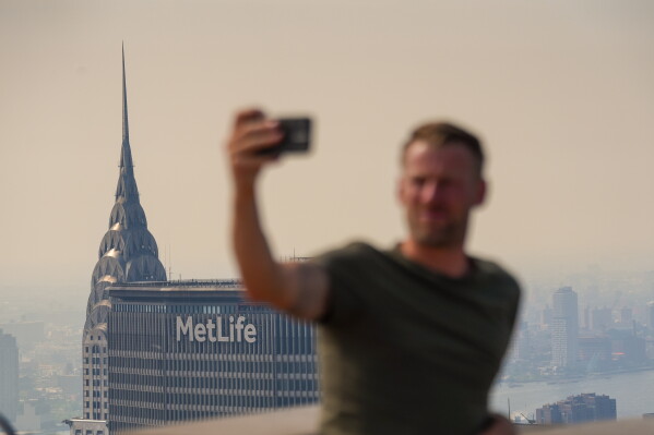A person takes a selfie from the Top of The Rock observation deck at the Rockefeller Center during an air quality health advisory due to wildfire smoke, in New York, Friday, July 17, 2026. (AP Photo/Ryan Murphy)