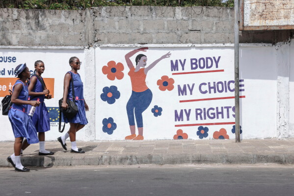 Schoolgirls walk home past a mural from the women's organization Plan International in Freetown, Sierra Leone, March 3, 2025. (AP Photo/Caitlin Kelly, File)