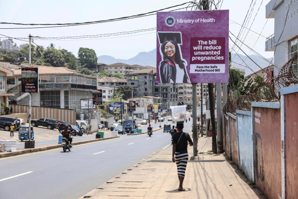 A woman walks past a billboard promoting the Safe Motherhood Bill on Wilkinson Road in Freetown, Sierra Leone, March 12, 2025. (AP Photo/Caitlin Kelly, File)