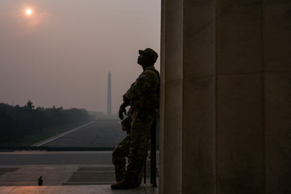 National Guardsmen patrol the Lincoln Memorial as the sun, obscured by wildfire smoke, rises above the Washington Monument and the Reflecting Pool, Friday, July 17, 2026, on the National Mall in Washington. (AP Photo/Julia Demaree Nikhinson)