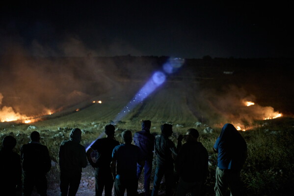 A Palestinian uses a flashlight after volunteers taking part in a night watch spotted Israeli settlers on a nearby hill and set brush ablaze to prevent them from approaching the West Bank village of Sinjil, Thursday, July 16, 2026. (AP Photo/Leo Correa)