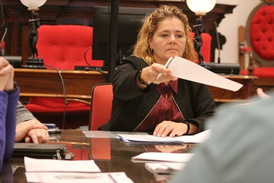 A woman in a blazer hands a piece of paper to someone next to her.
