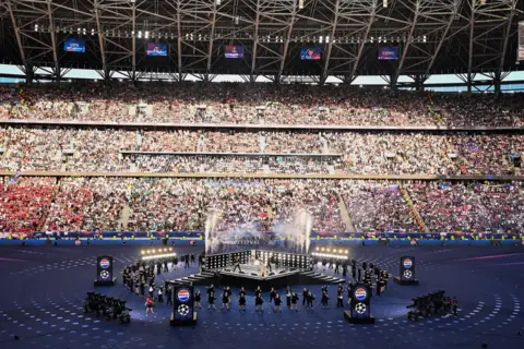 Live Nation/ Getty Images Picture of the stage at the Puskas Arena, Budapest. A large stand of crowds is seen in the backgorund of a stage in the middle of the pitch.