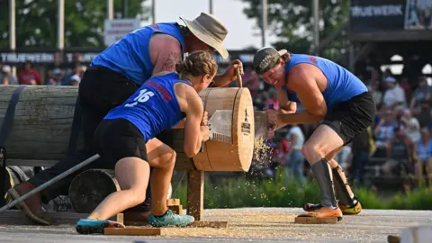Lumberjack World Championships Two women brace themselves and crouch on either side of a huge wooden log while using a double-handled saw to slice through it