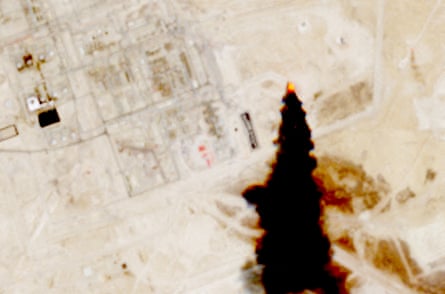 Black smoke trails across the picture from an oil facility in a desert landscape