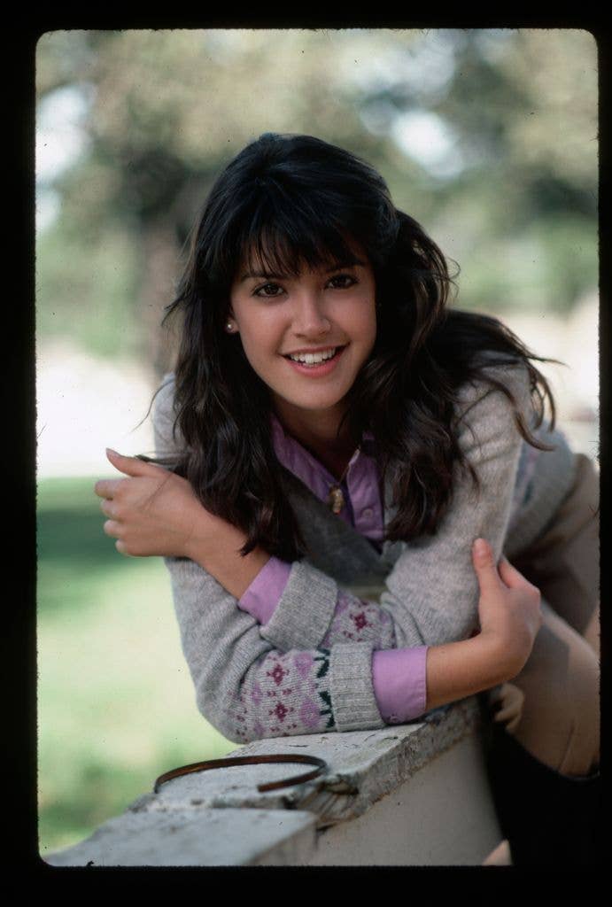 Outdoor portrait of actress Phoebe Cates. She is shown waist-up, resting her crossed arms on a wooden fence, dated 1982.