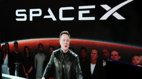 Reuters Elon Musk appearing via video stream wearing a black leather jacket an speaking at a podium upon the June debut of his company SpaceX on the Nasdaq stock exchange.