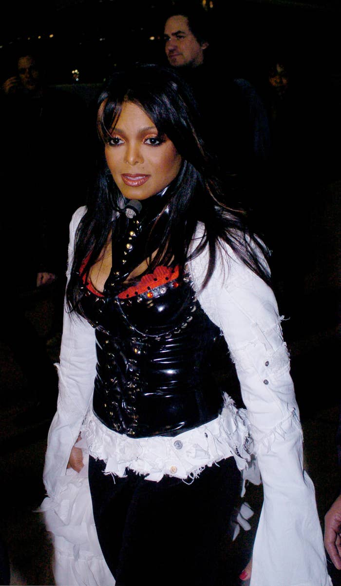 Janet Jackson walking, wearing a distinctive gothic-style outfit with a corset over a distressed long sleeve top
