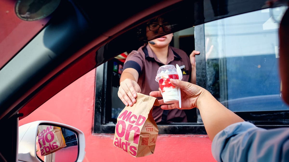 A McDonald's employee hands food to a customer at a drive-thru window.