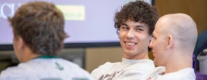 A young man smiles at another whose back is to the camera.