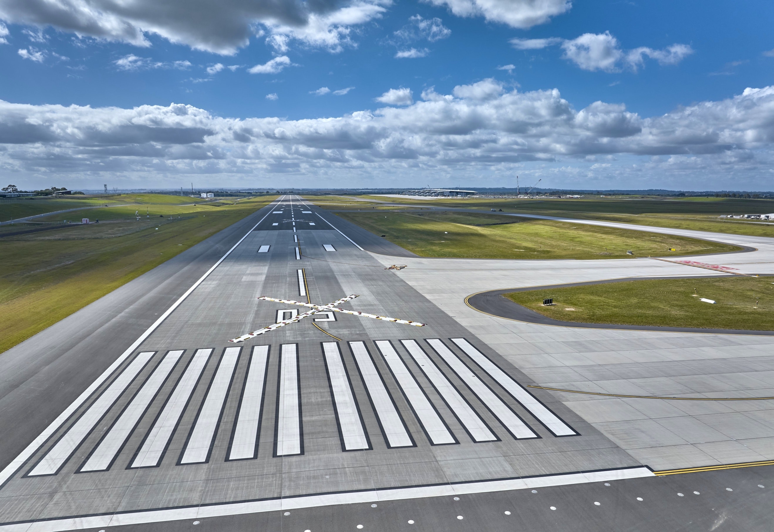 An aerial view of an airport runway with white striped markings and the number