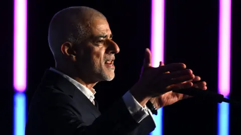 Getty Mayor of London Sir Sadiq Khan delivers a speech during London Tech Week. He is pictured speaking into a microphone with his hands open either side of the microphone.