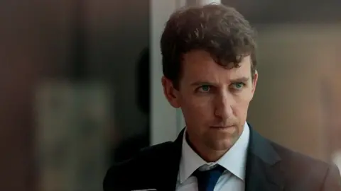 REUTERS/Brian Snyder A man with brown curly hair and a dark suit, white shirt and blue tie is seen looking away from the camera with a serious expression. It is a close-up shot and he appears serious.