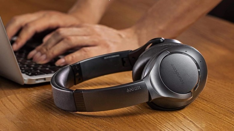 The Anker Soundcore Life Q20 headphones, placed on a wooden surface next to a laptop, with a pair of hands typing on it