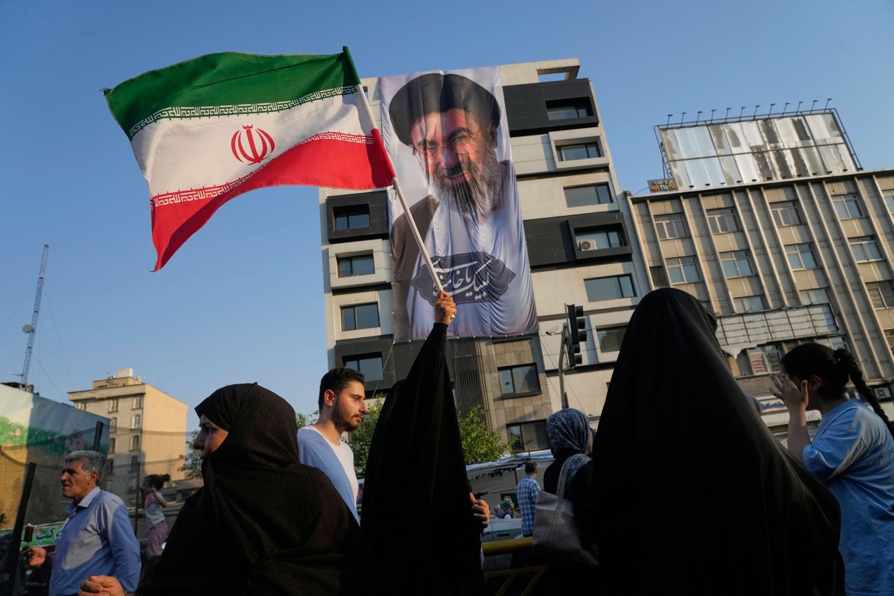 A woman holds up an Iranian flag in front of a banner bearing a portrait of Iran's Supreme Leader, Ayatollah Mojtaba Khamenei, during a street festival celebrating the Shiite Muslim holiday of Eid al-Ghadir in Tehran on June 4.