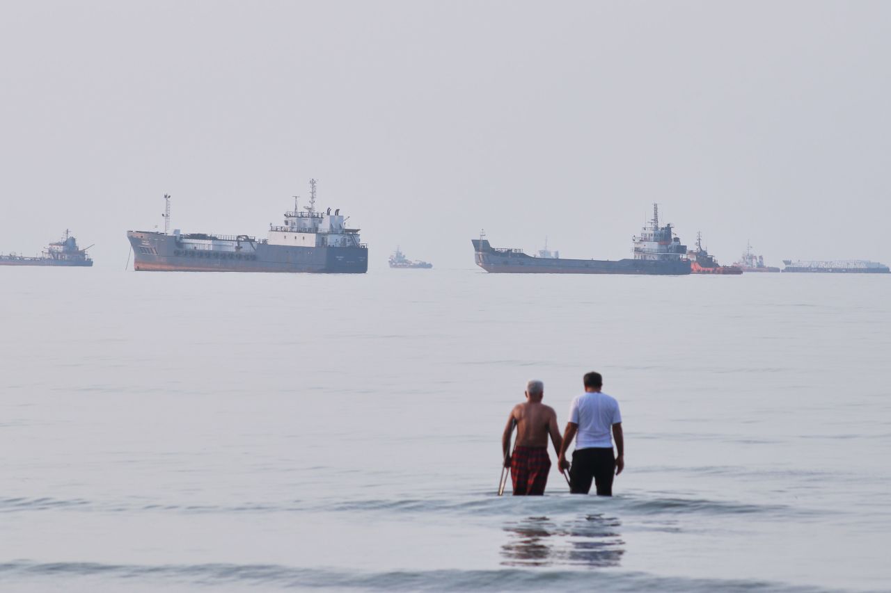 Two men wade in the waters of the Strait of Hormuz with vessels anchored in the background, off Bandar Abbas, Iran, Sunday, July 12.