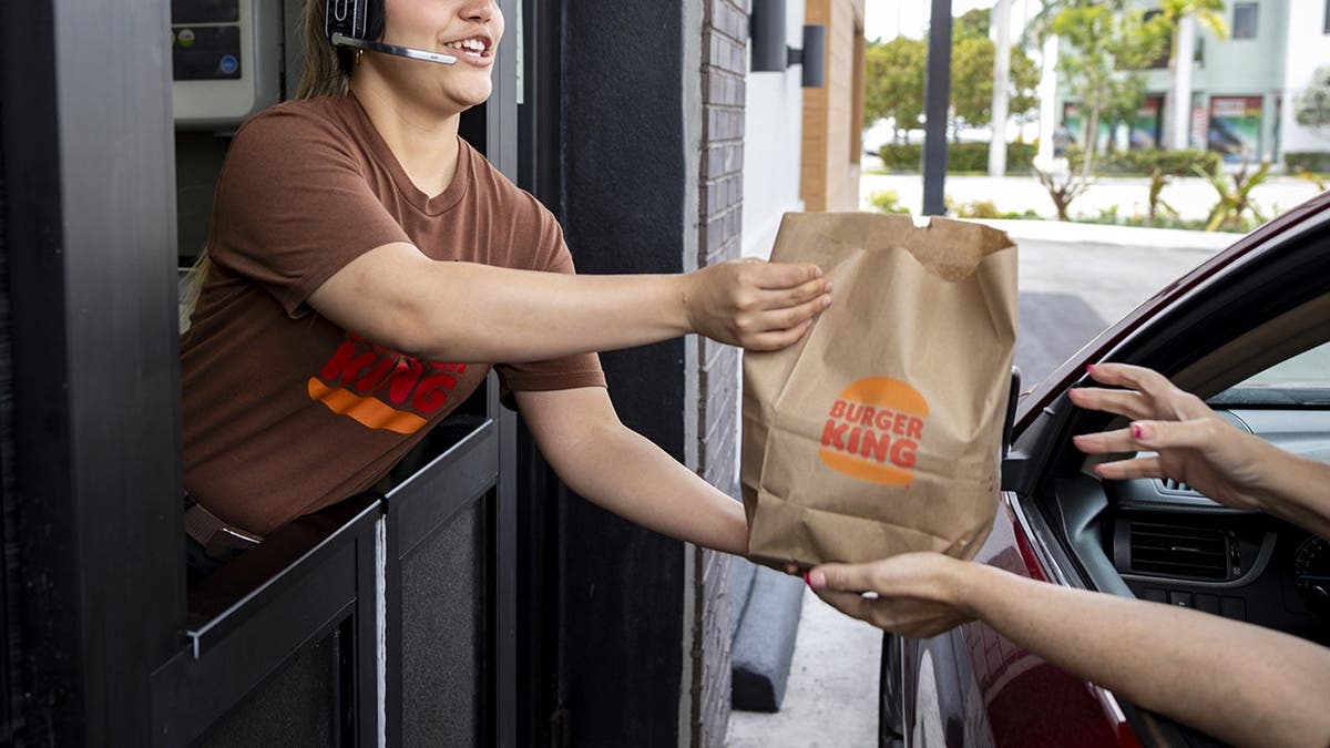 A Burger King employee hands a bag of food to a customer at a drive-thru.
