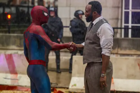 Marvel/ Sony Pictures Entertainment Spiderman shaking hands with a man in a waistcoat, shirt, tie and trousers.