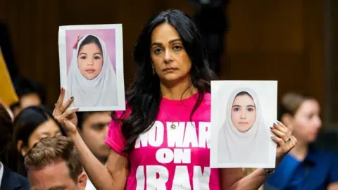 Reuters Protesters hold up pictures of Iranian girls at the Senate hearing for Secretary of Defense Pete Hegseth on 21 July 2026