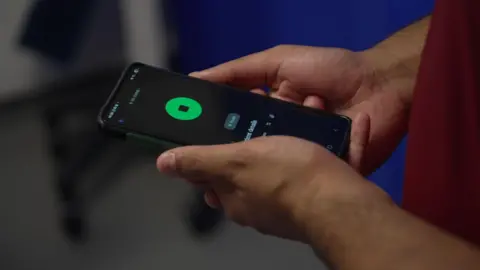 BBC A doctor holding a mobile phone with a recording app open