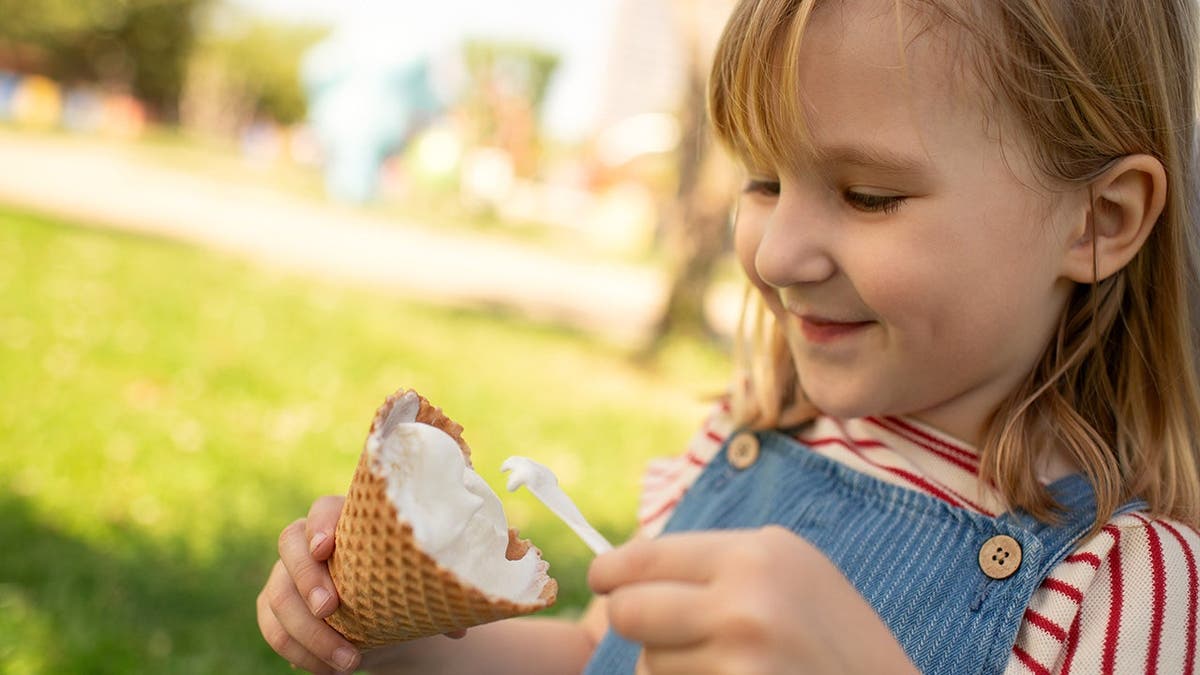 A child uses a spoon to eat a dish of vanilla ice cream.