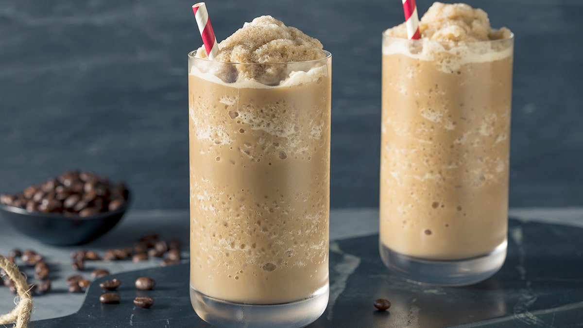 Two frozen coffee slushies are pictured in tall glasses with red-and-white-striped straws.