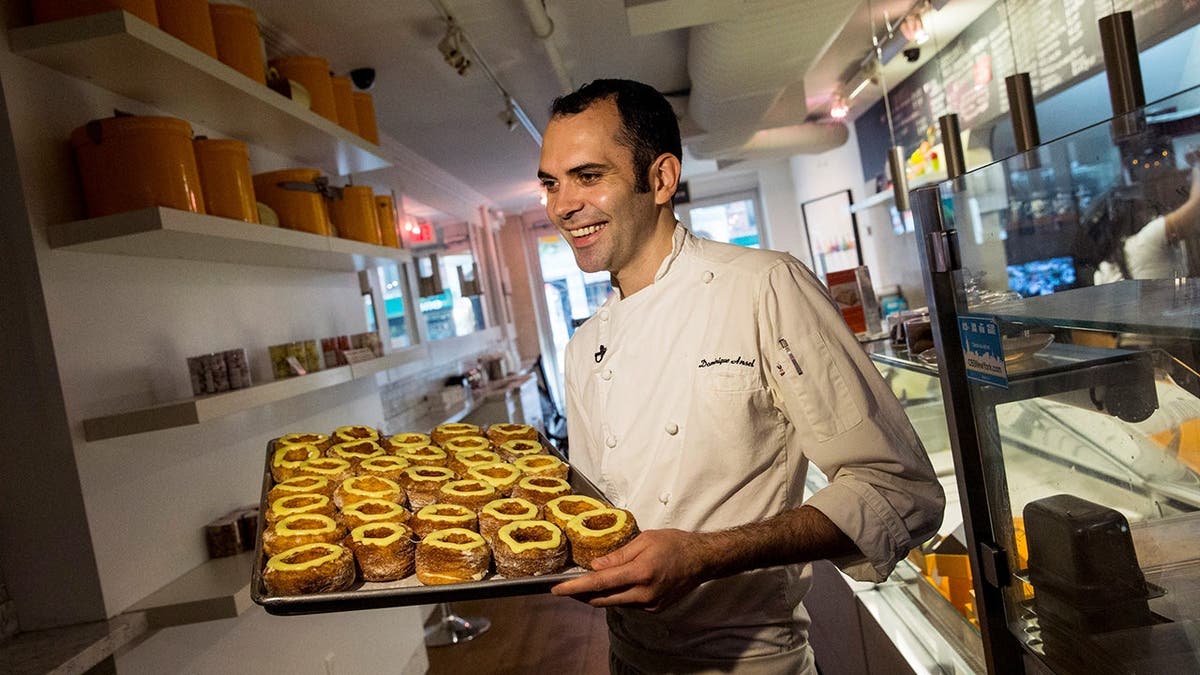 A man carries a tray of cronuts.