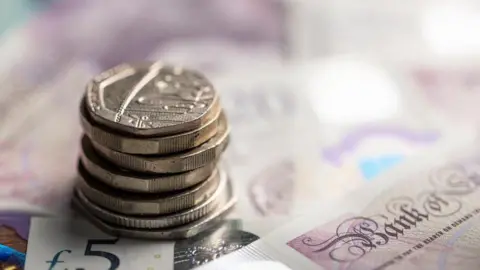 Getty Images A pile of coins on top of Bank of England notes
