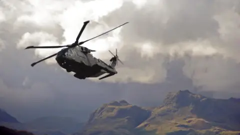 iStock An RAF helicopter above a mountain range - it flies low to the cliff face against a dramatic grey cloud.