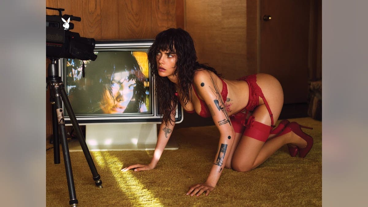 Cara Delevingne wearing red, kneeling in a wide shot.