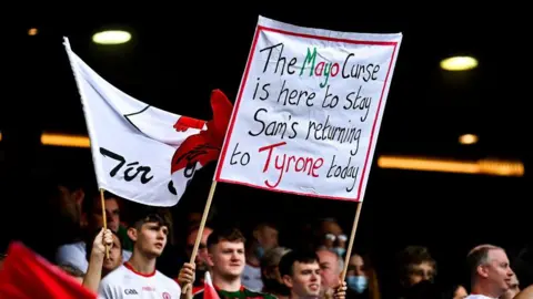 Getty Images A crowd of people. One of the people is holding a large banner which reads: 'The Mayo Curse is here to stay Sam's returning to Tyrone today'.