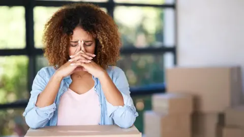 Getty Images A woman with her head in her hands surrounded by boxes
