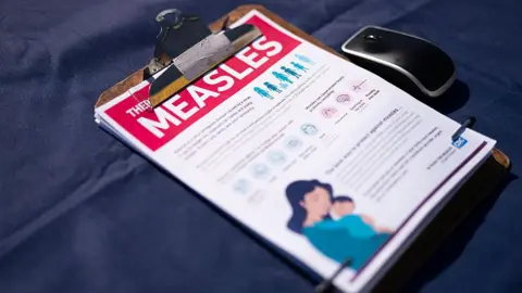 Getty Images A fact sheet for measles sits on a table with a dark blue tablecloth, in a clipboard