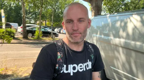BBC A man is wearing a black t shirt standing under neath a tree.