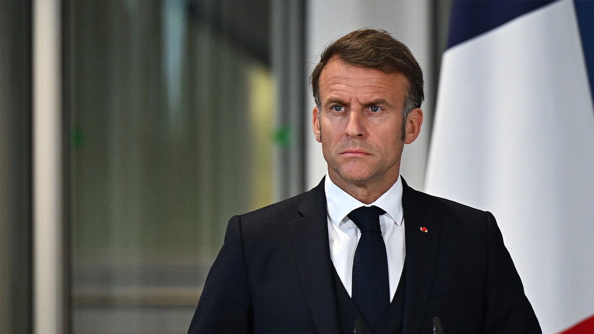 French President Emmanuel Macron in black suit standing at podium