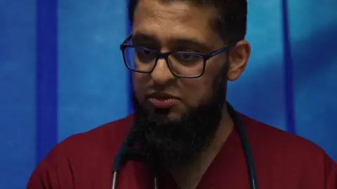 A male doctor talking to a patient. he is wearing red scrubs