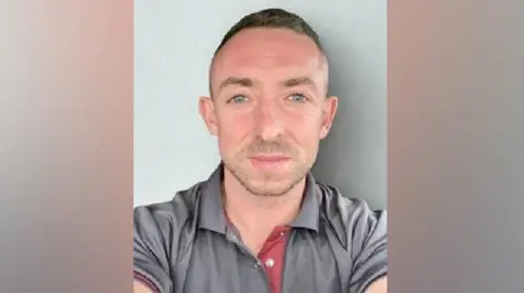 University Hospitals Sussex John Gault. He has short hair, blue eyes and is wearing a grey polo shirt