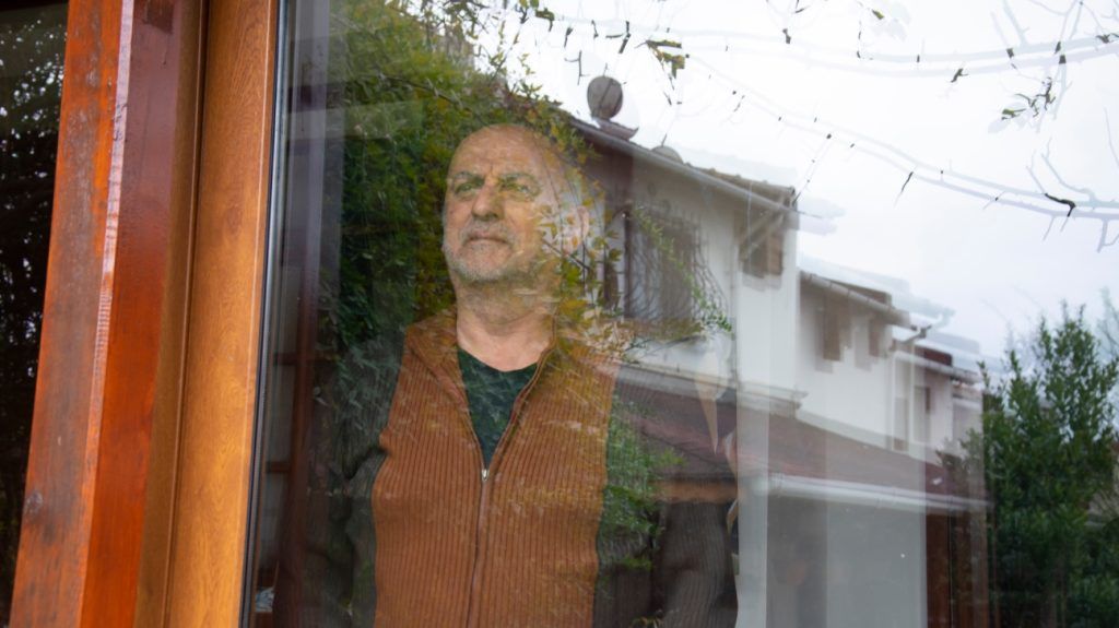 An older adult man with dementia looks out of a window