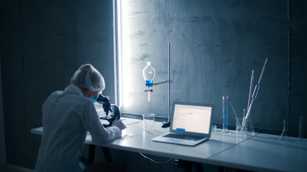 scientist conducted research in laboratory at the microscope next to pipette and laptop