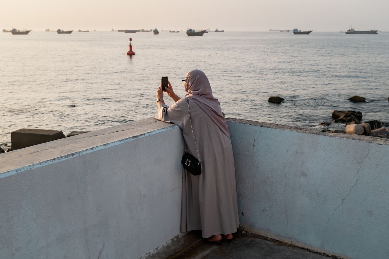 A woman photographs Qaboos Port where oil tankers, carriers, vessels and Omani fisherboats sit anchored in Muscat, Oman, on June 19.