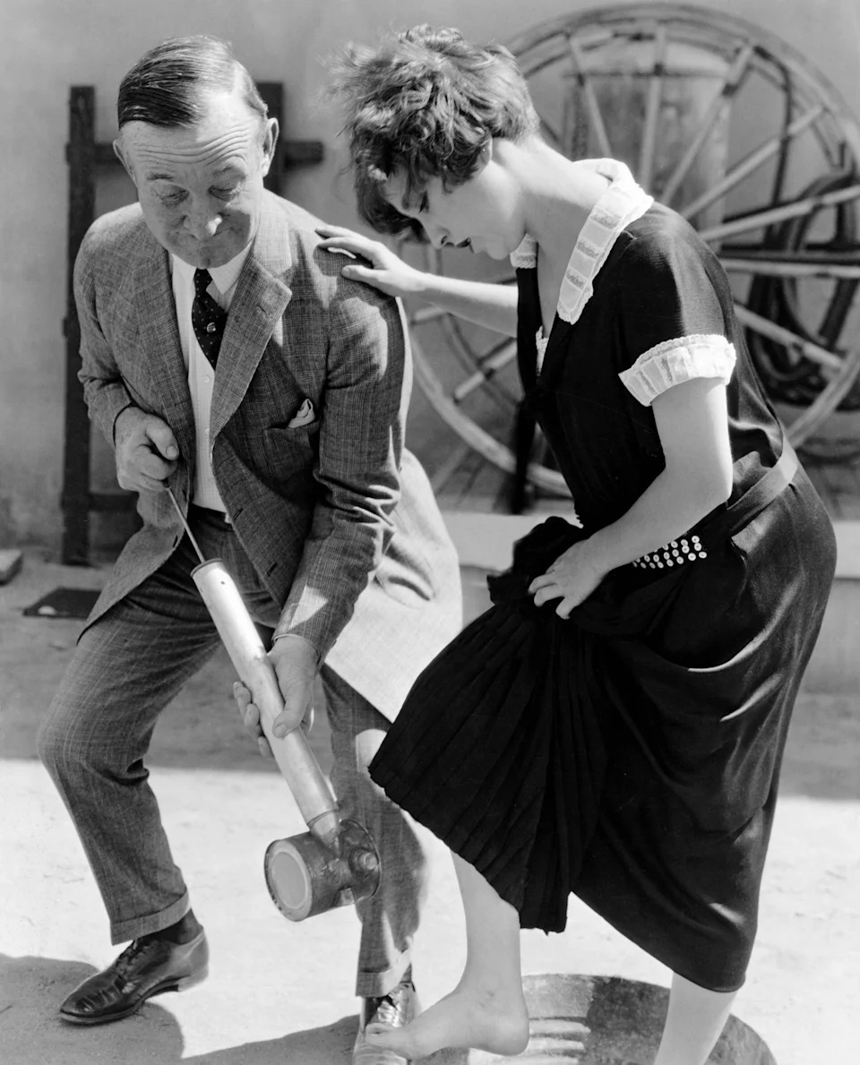 Charlie Murray sprays Bessie Love's foot with an old-fashioned instrument