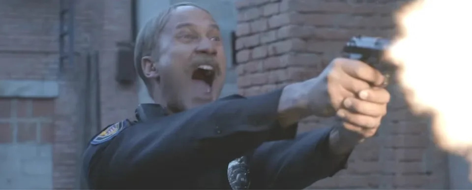 A person in a police uniform is energetically firing a handgun in an action scene, with a dramatic expression on their face
