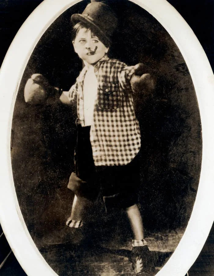 Mickey Rooney in vintage boxing outfit, including gloves and checkered shirt, poses confidently with a playful stance