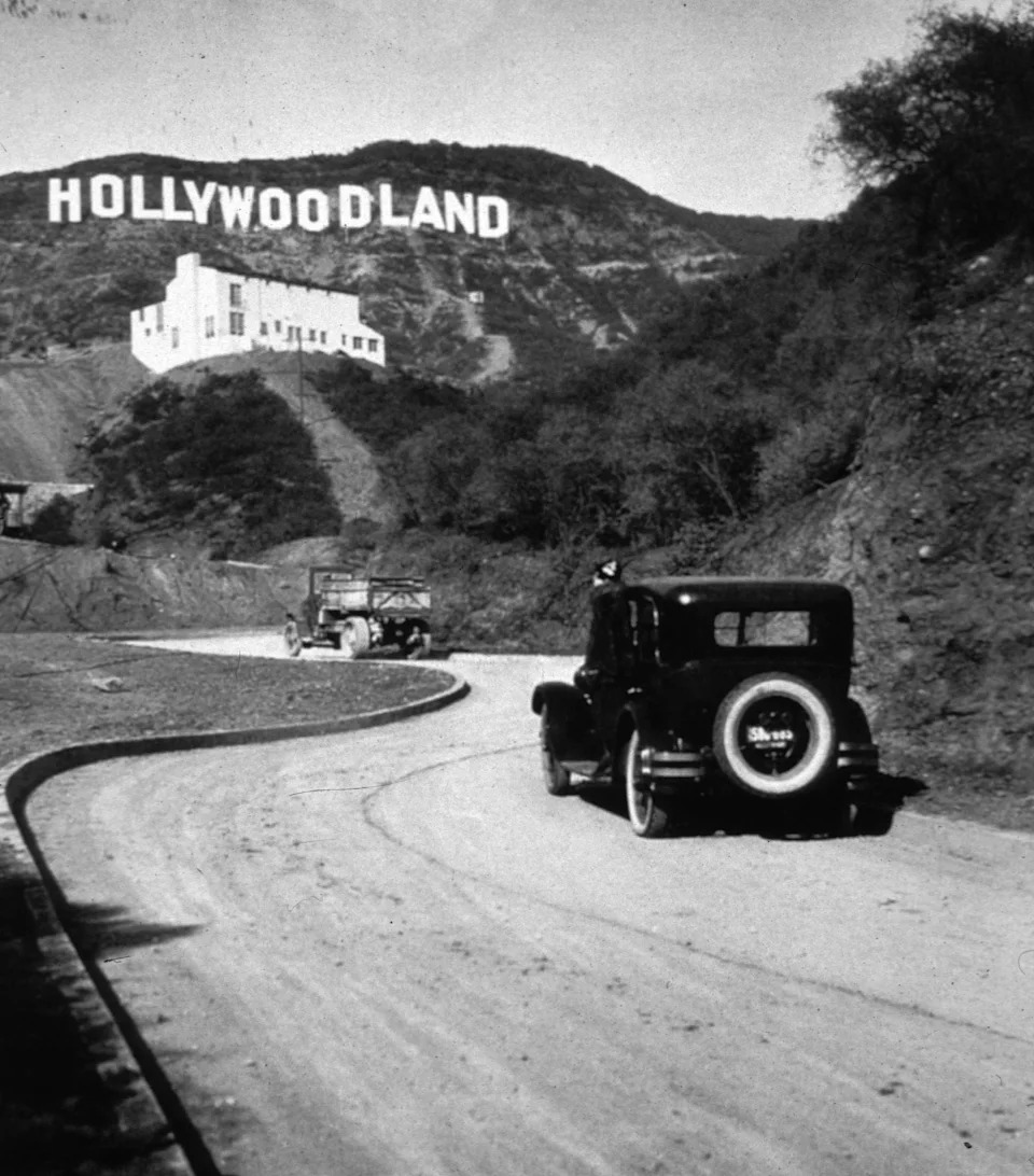 Vintage cars drive toward the original Hollywoodland sign situated on a hillside